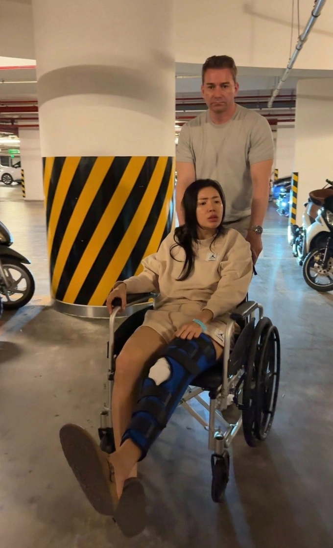 Minh Tú ngồi xe lăn trong bãi đỗ xe sau tai nạn, thể hiện quá trình hồi phục